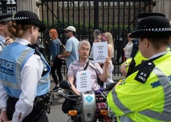 Disabled man Neil Goodwin protesting in his mobility scooter at the entrance to parliament. He is surrounded by police officers and holding signs that read "disabled people against climate change" and ""I cannot run from a climate emergency"