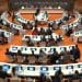 UNCRPD forum room at Geneva there are circles of long tables with people sitting at screens at the top of the room is a long table against a marble stone backdrop