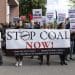 Protesters outside Glencore's AGM gather with a large banner that reads: Stop coal now! Clean up your mess! Respect human rights! Just transition for workers and communities! Others carry placards. One in English reads: Stop fueling genocide Israel