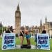 LUSH and EachOther activists stage a shower protest in parliament square. Two activists stand having a shower in their swimming costume and trunks, while others hold a shower head over them and big box mock ups of LUSH's 'human rights' product that reads: "human rights for everyone"