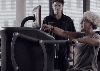 Lady uses EGYM equipment with an EGYM trainer behind long Covid exercise programme Northamptonshire