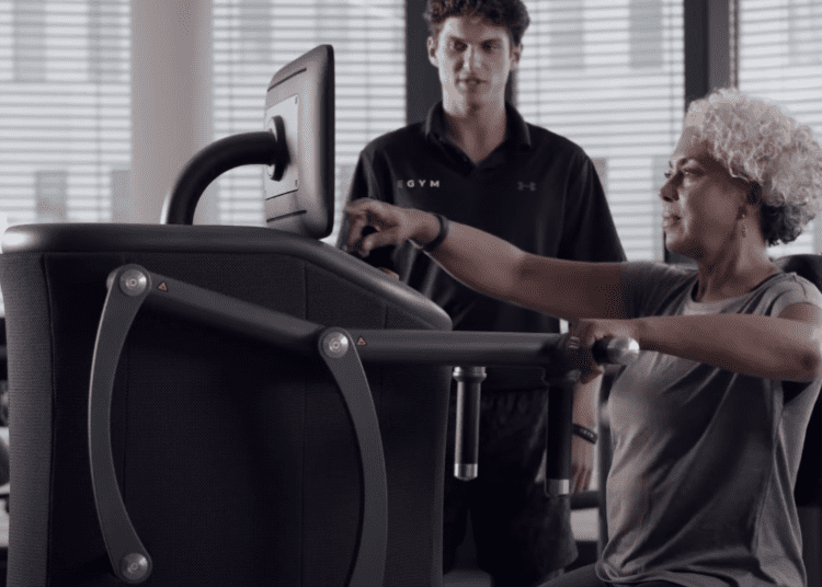 Lady uses EGYM equipment with an EGYM trainer behind long Covid exercise programme Northamptonshire