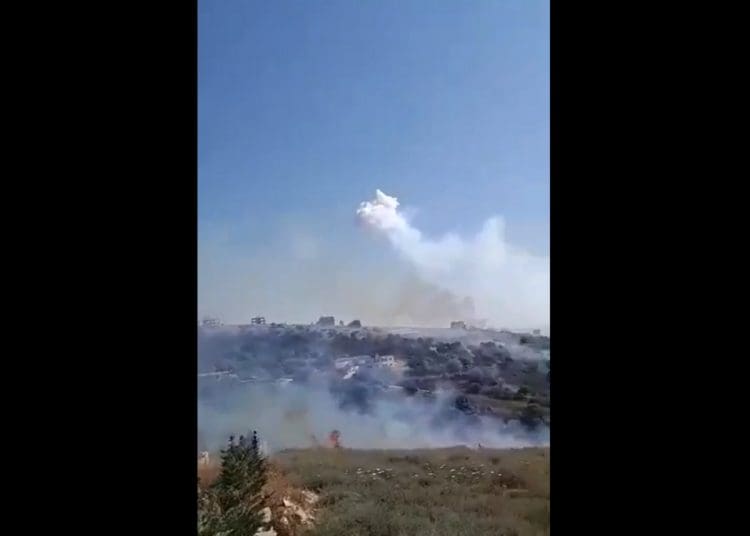 Israel bombing Lebanon with white phosphorus. White smoke and flames rise from an area of grassy hills and trees, with a few houses interspersed between World Environment Day ecocide