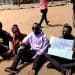 Ugandan anti-corruption protesters sit on the ground with placards.