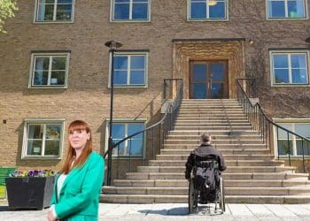 Labour housing policy a male wheelchair user at the bottom of a flight of outside steps leading up to a block of flats with Angela Rayner in a turquoise suit looking at the camera