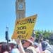 Paula Peters holding a yellow placard that reads in black writing "accessible social homes now" with Big Ben in the background. It is a sunny day at a protest over accessible housing