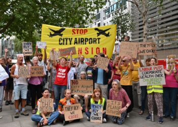 Protesters gather with banners and placards which read: "Stop City Airport Expansion", "Revoke the decision", "They fly, we choke", and "Ban expansion, not protest" London City Airport Labour