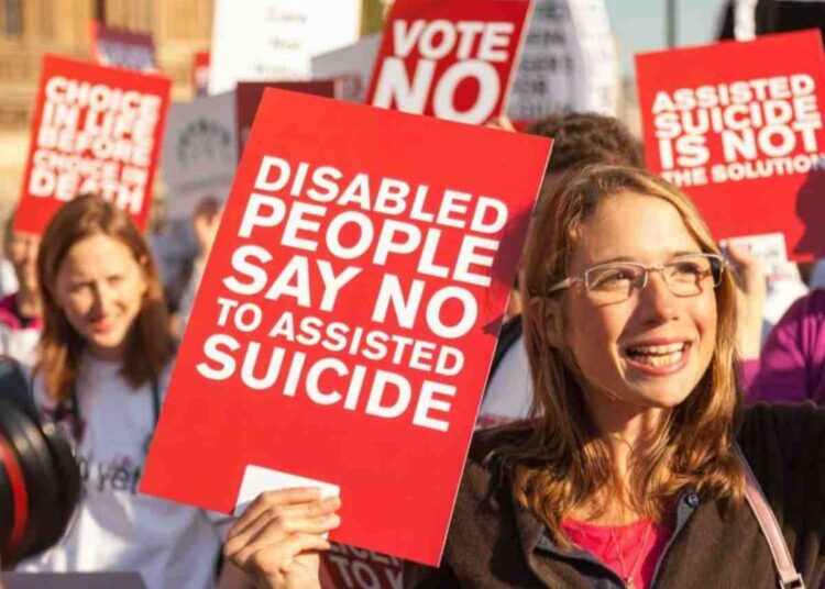 a protester holding a sign saying "disabled people say no to assisted suicide" assisted dying
