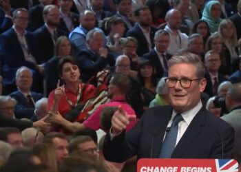 Keir Starmer pointing from his podium which reads: "Change begins" as a protester in a crowd speaks out, with security guards preparing to remove him Labour Palestine