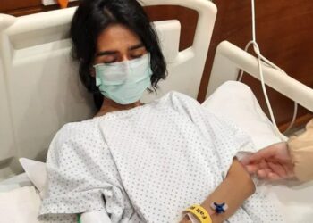 Severe ME/CFS patient Nevra in a hospital bed with her eyes closed, wearing a face-mask, and IV cannula attached to her wrist Pakistan