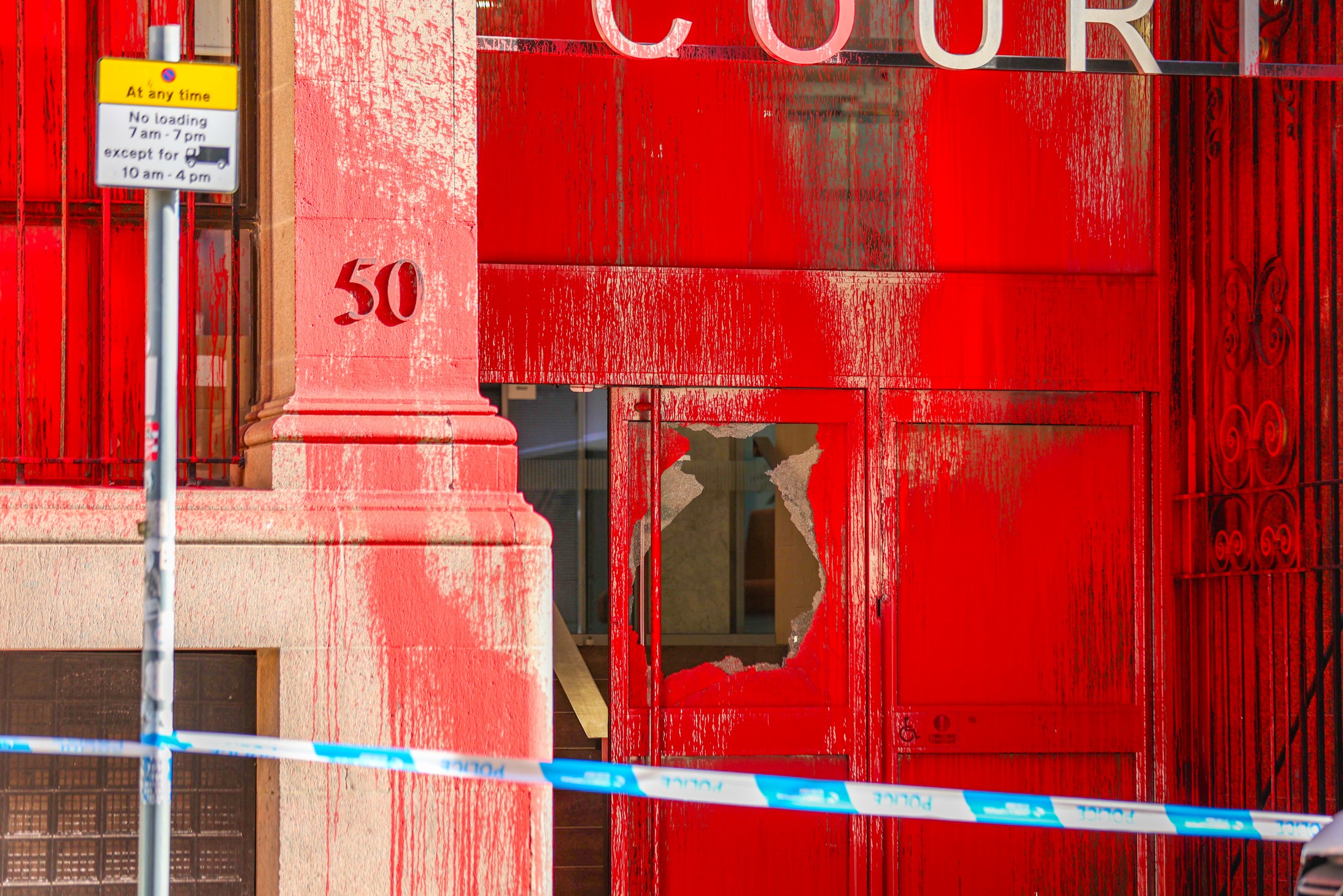 Atrium Court, Glasgow, covered in red paint, with a broken glass door. Police cordon tape stretches out in front.