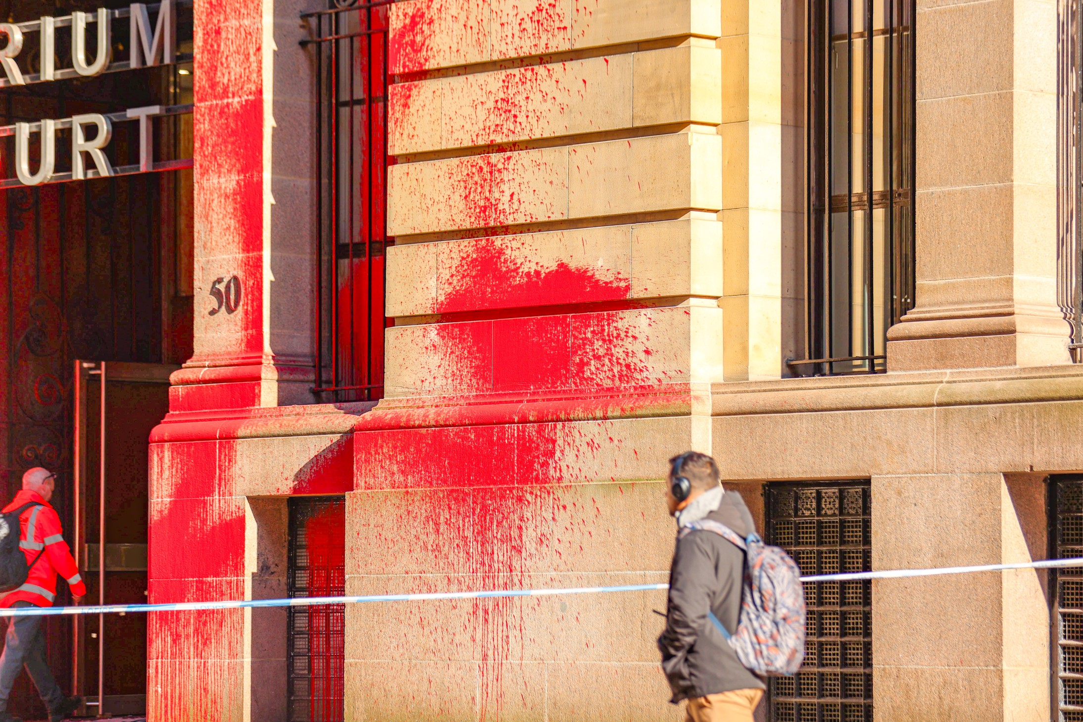 Red paint up the walls of the Atrium Court entrance in Glasgow, as a person walks by Scottish Enterprise Palestine Action