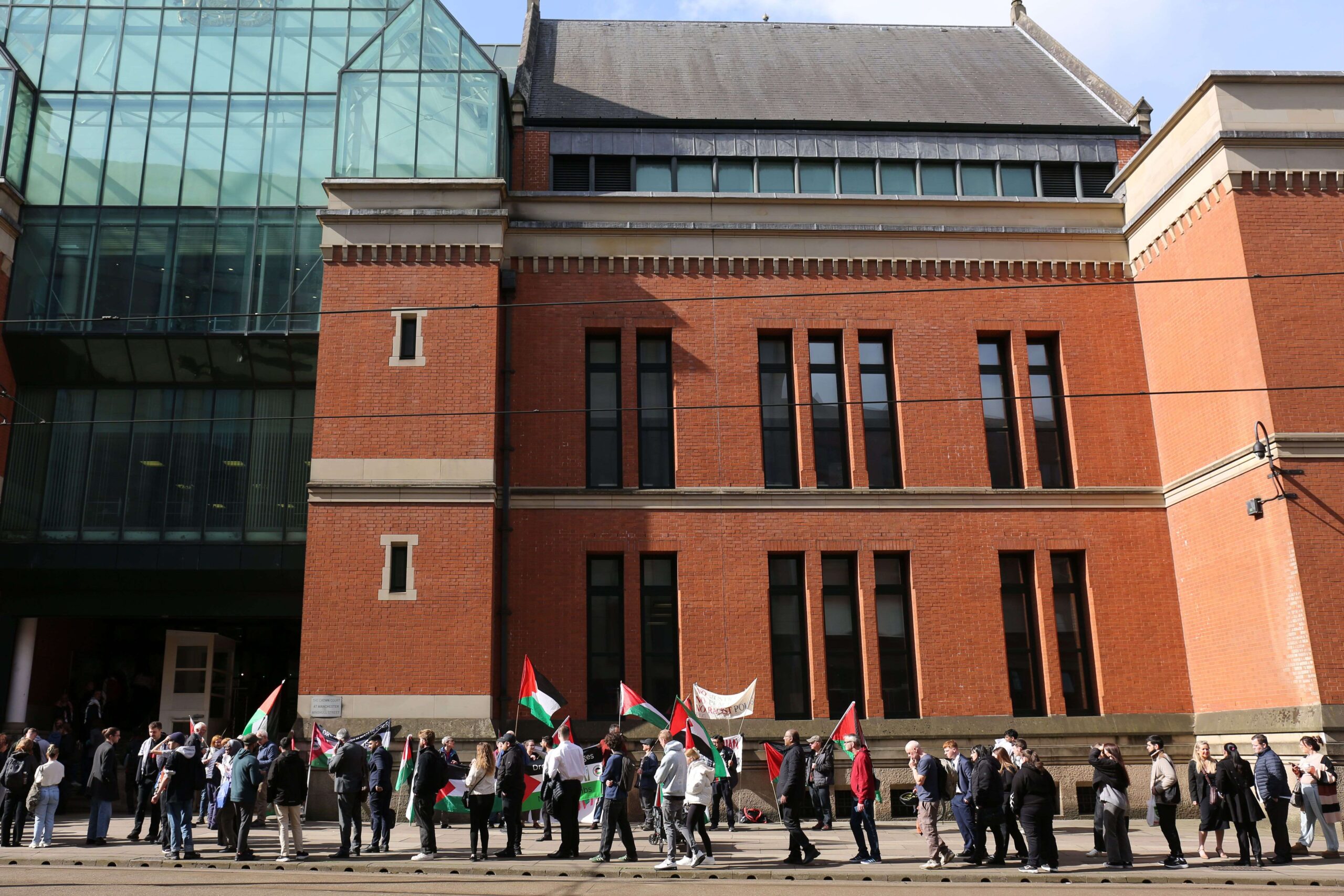 Large crowd gathers with Palestine flags outside Manchester Crown Court.