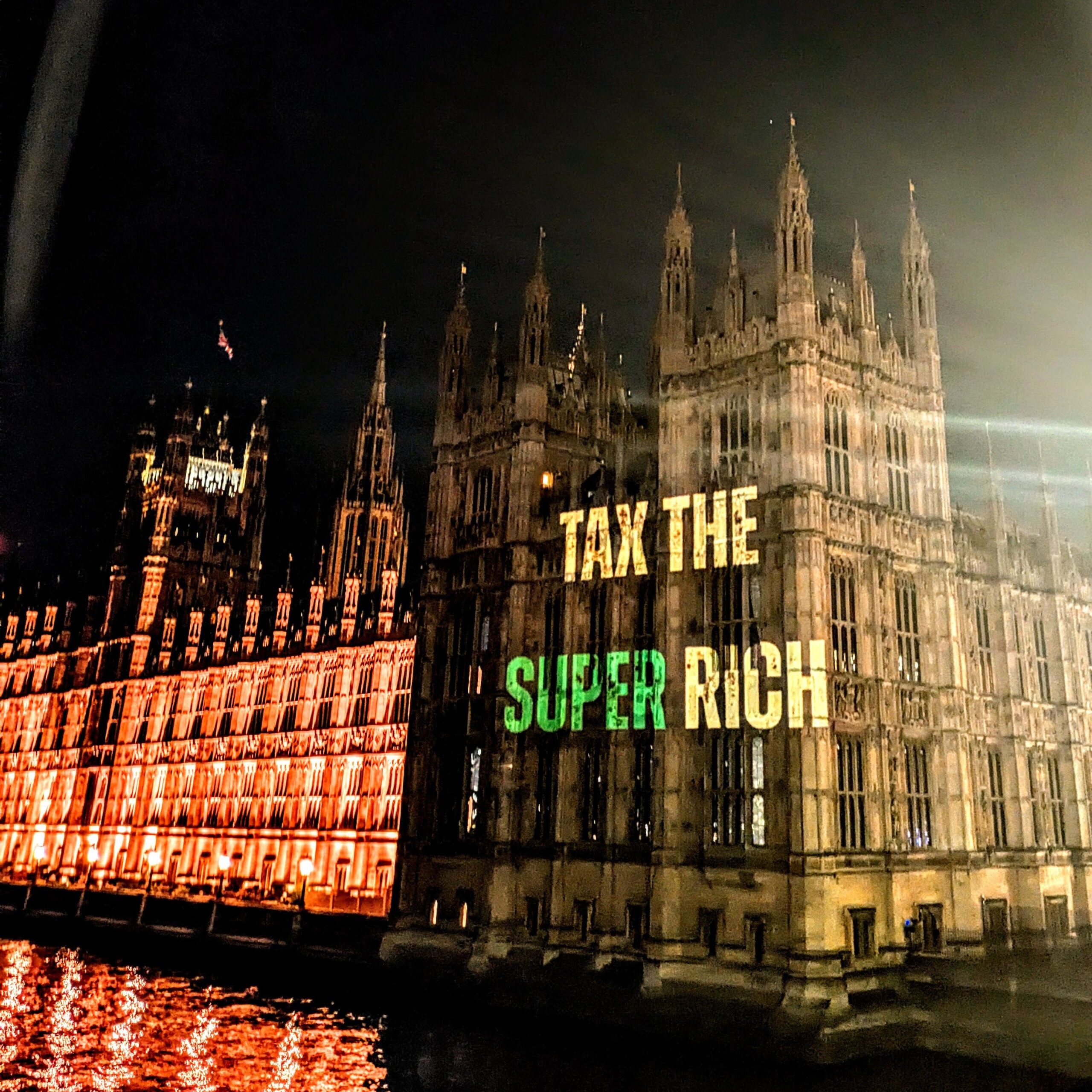 Projection on parliament that reads "Taz the super rich" in white and green text. 