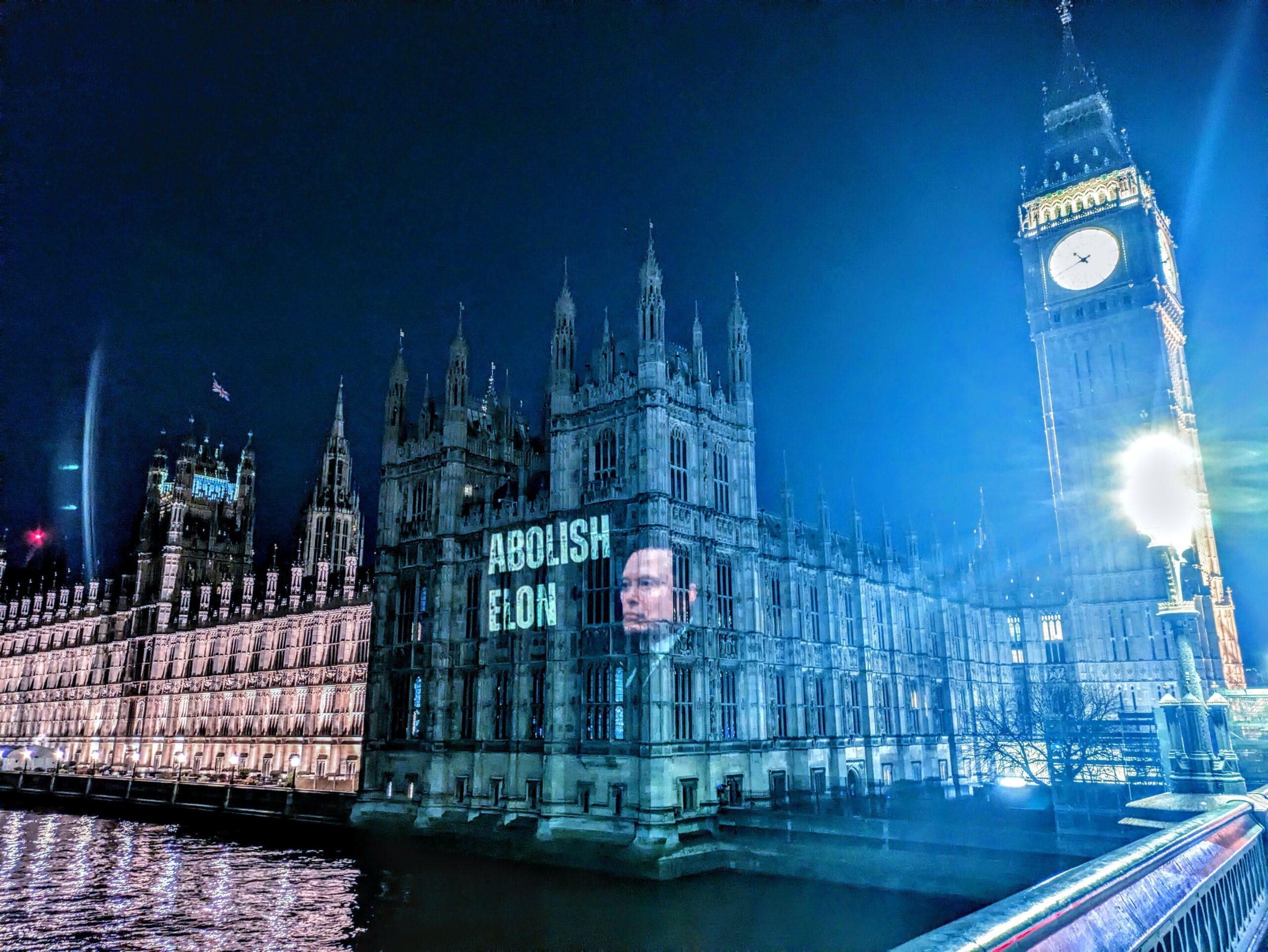 Projection of Elon Musk's face on parliament, with Big Ben in the background, and the words: "Abolish Elon" in bold white text. 