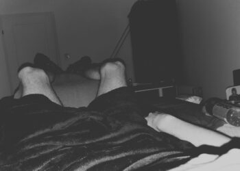 Man's legs raised in bed, with a blanket, and electrolyte sports drinks to his side ME/CFS