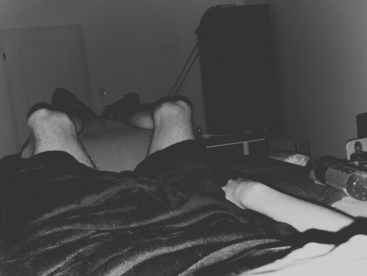 Man's legs raised in bed, with a blanket, and electrolyte sports drinks to his side ME/CFS