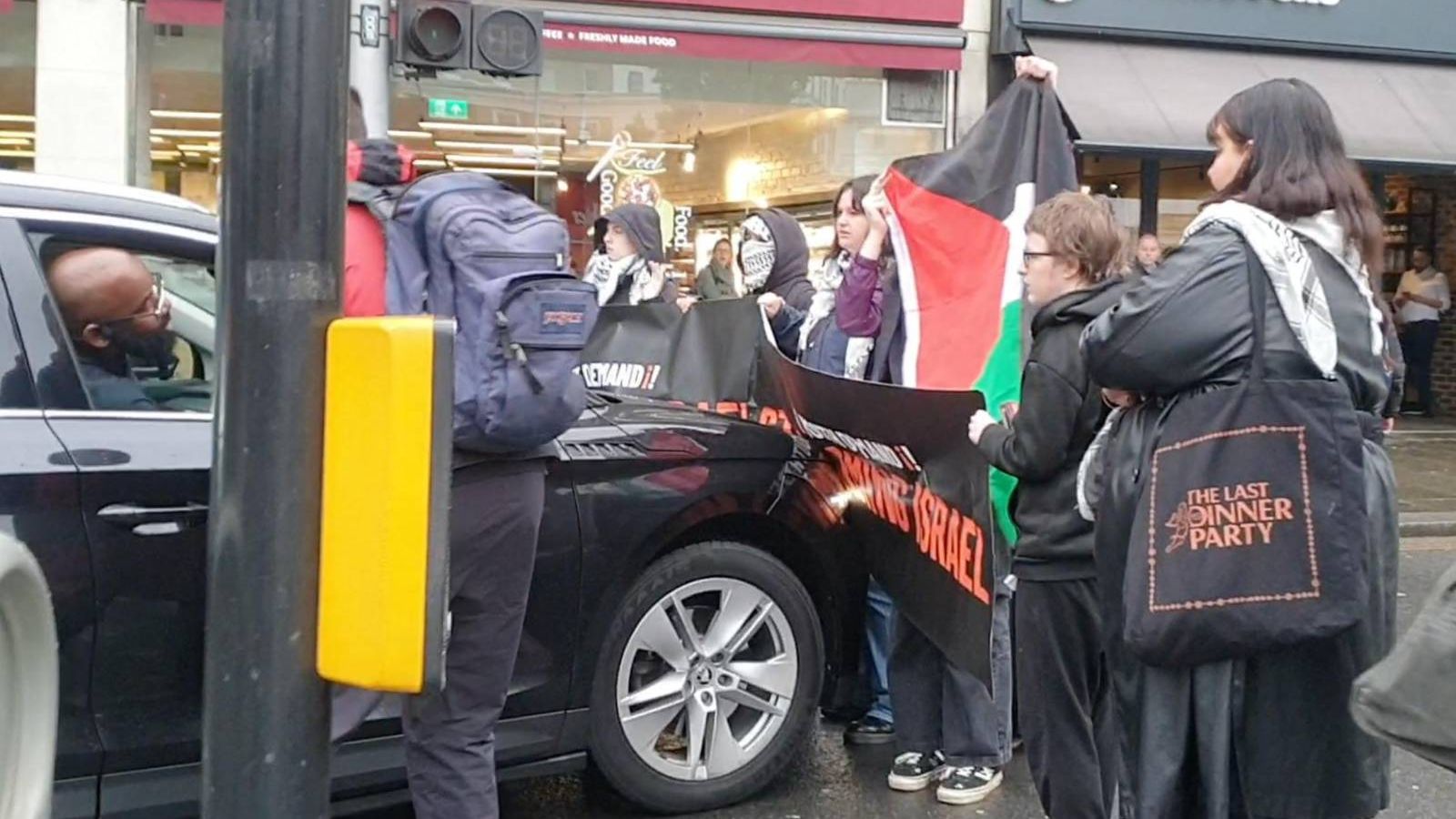 Youth Demand activists with a Palestine flag and banners block the road to oncoming traffic. 