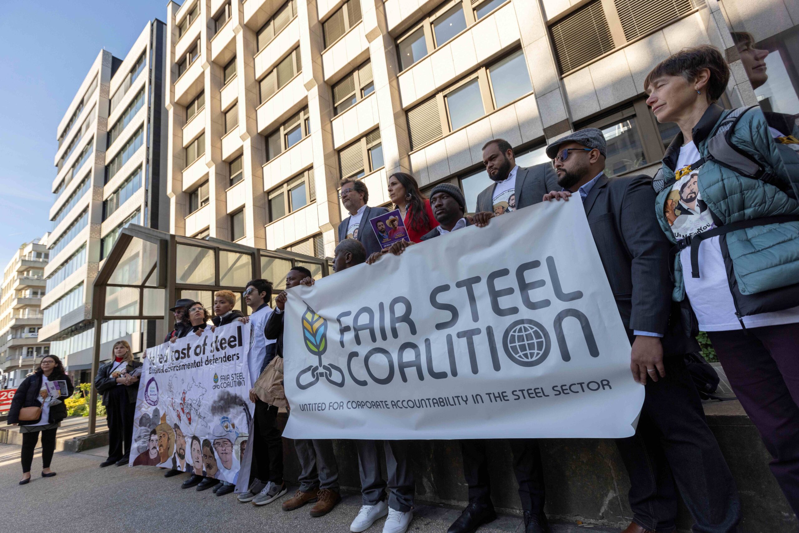 Protesters stand in a line with banners reading: "The real cost of steel: disappeared environmental defenders" and "Fair Steel Coalition". 