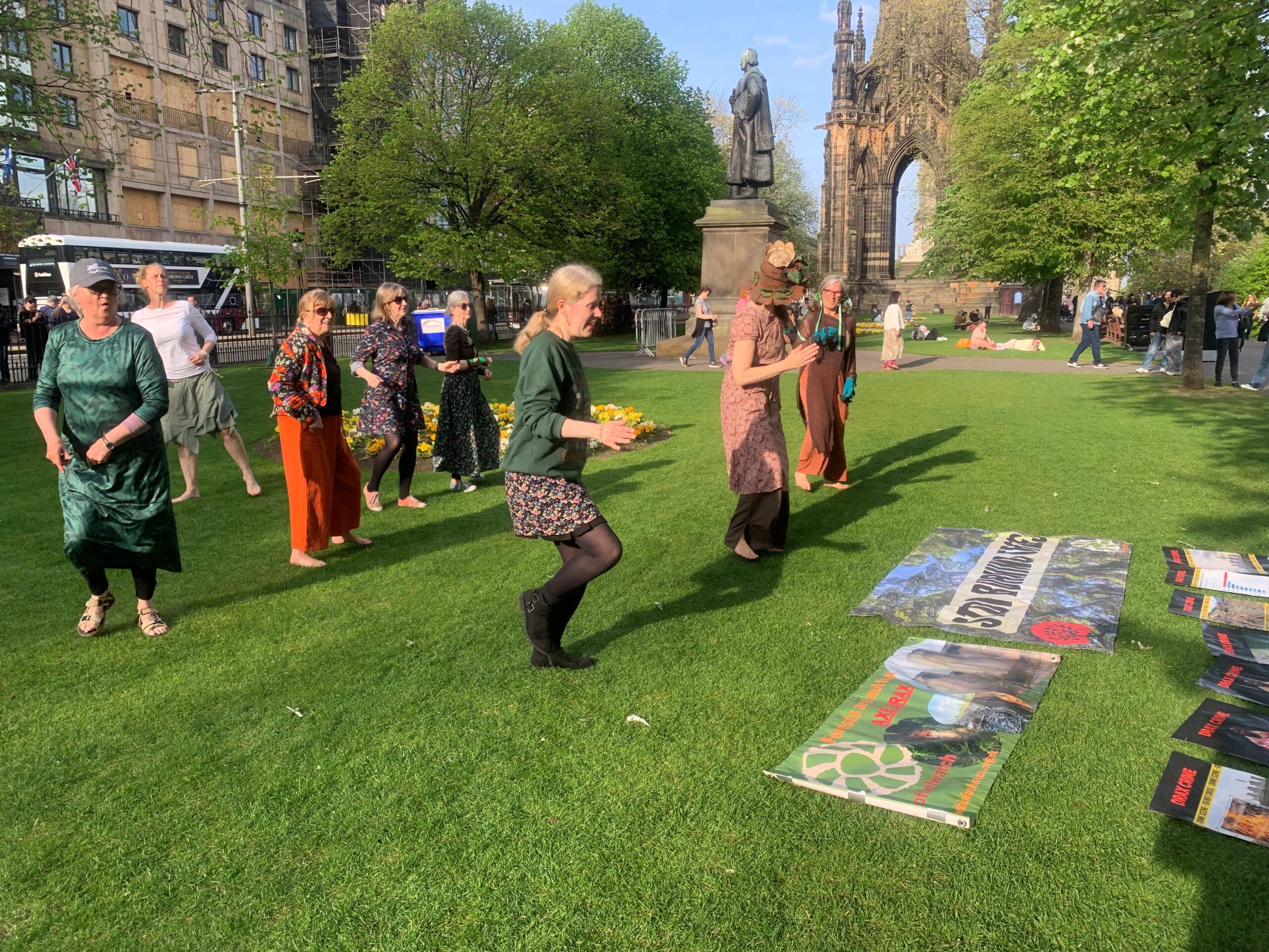Campaigners dance together in Princes Street Gardens, in front of banners laid out on the grass. 