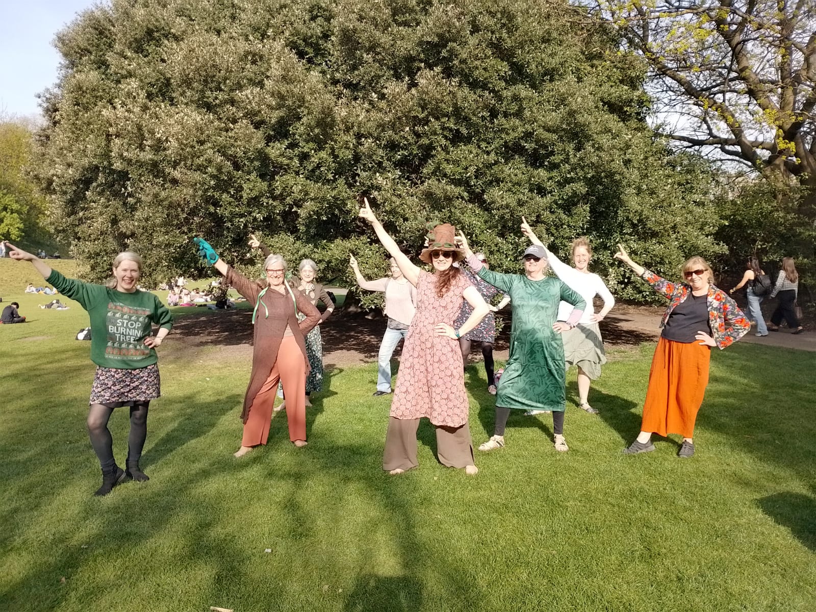 Nine women strike a pose while dancing on the grass, with trees behind, in Princes Street Gardens, Edinburgh. 