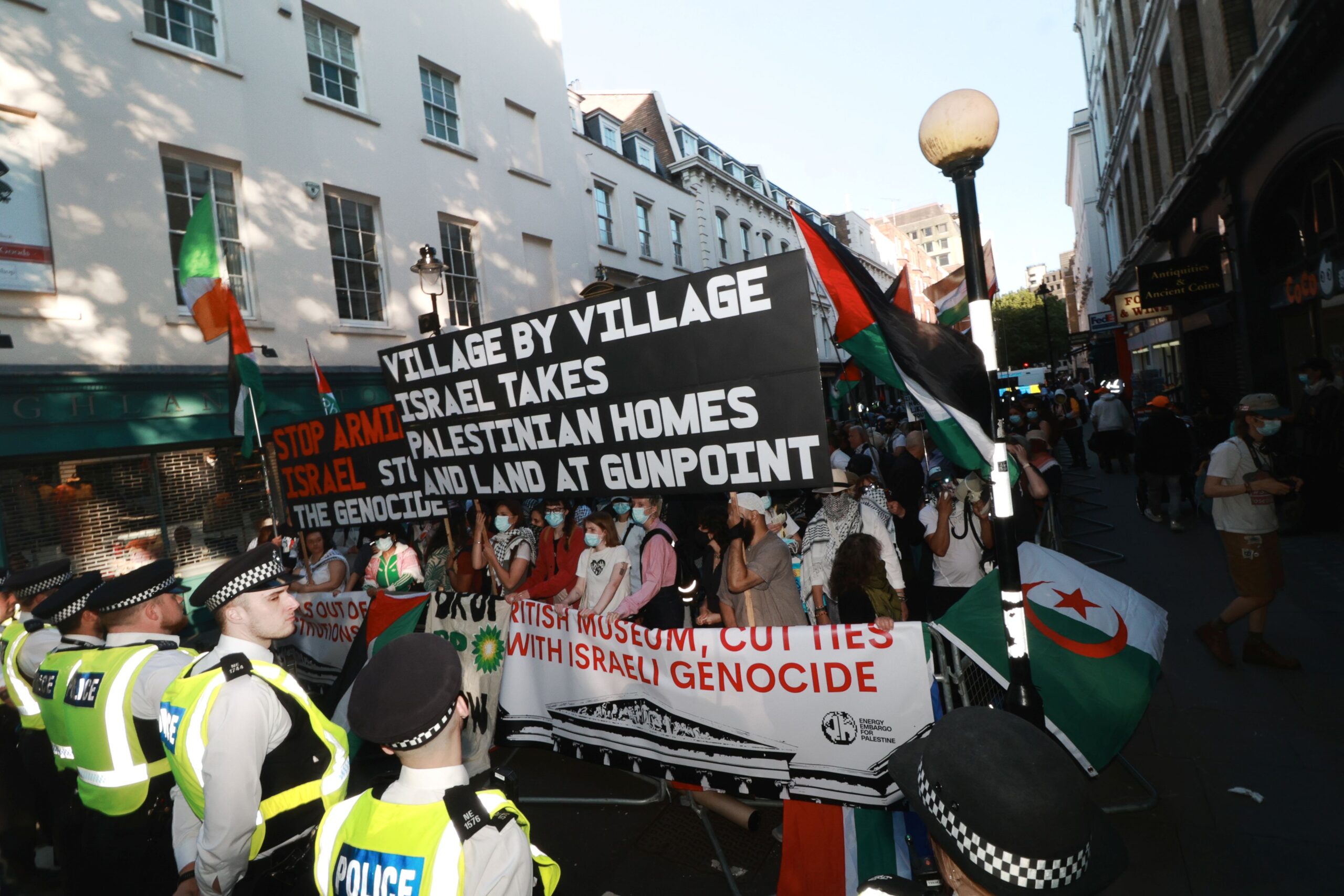 Protesters holding banners reading “British Museum, cut ties with Israeli genocide” and “War criminals out of public institutions” in front of the British Museum with a line of police before them. 