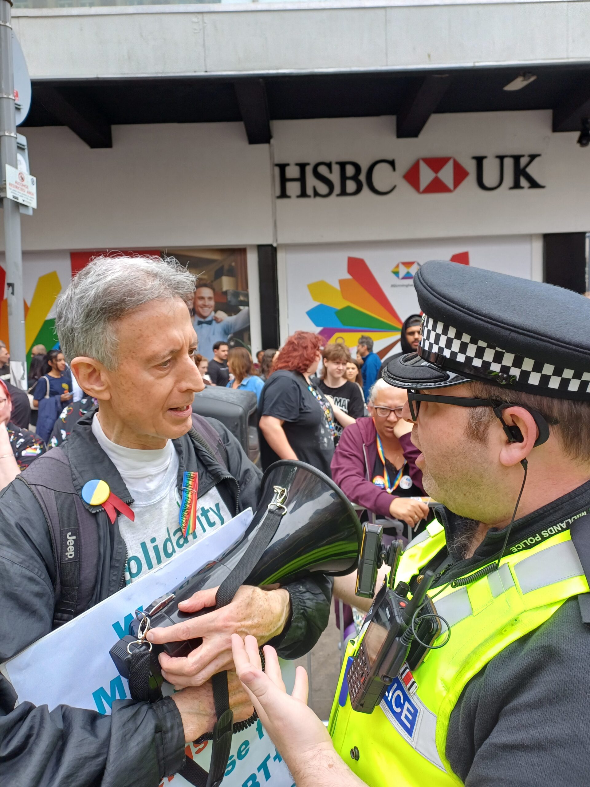 Police officer talking to Peter Tatchell who is holding a placard and megaphone. 