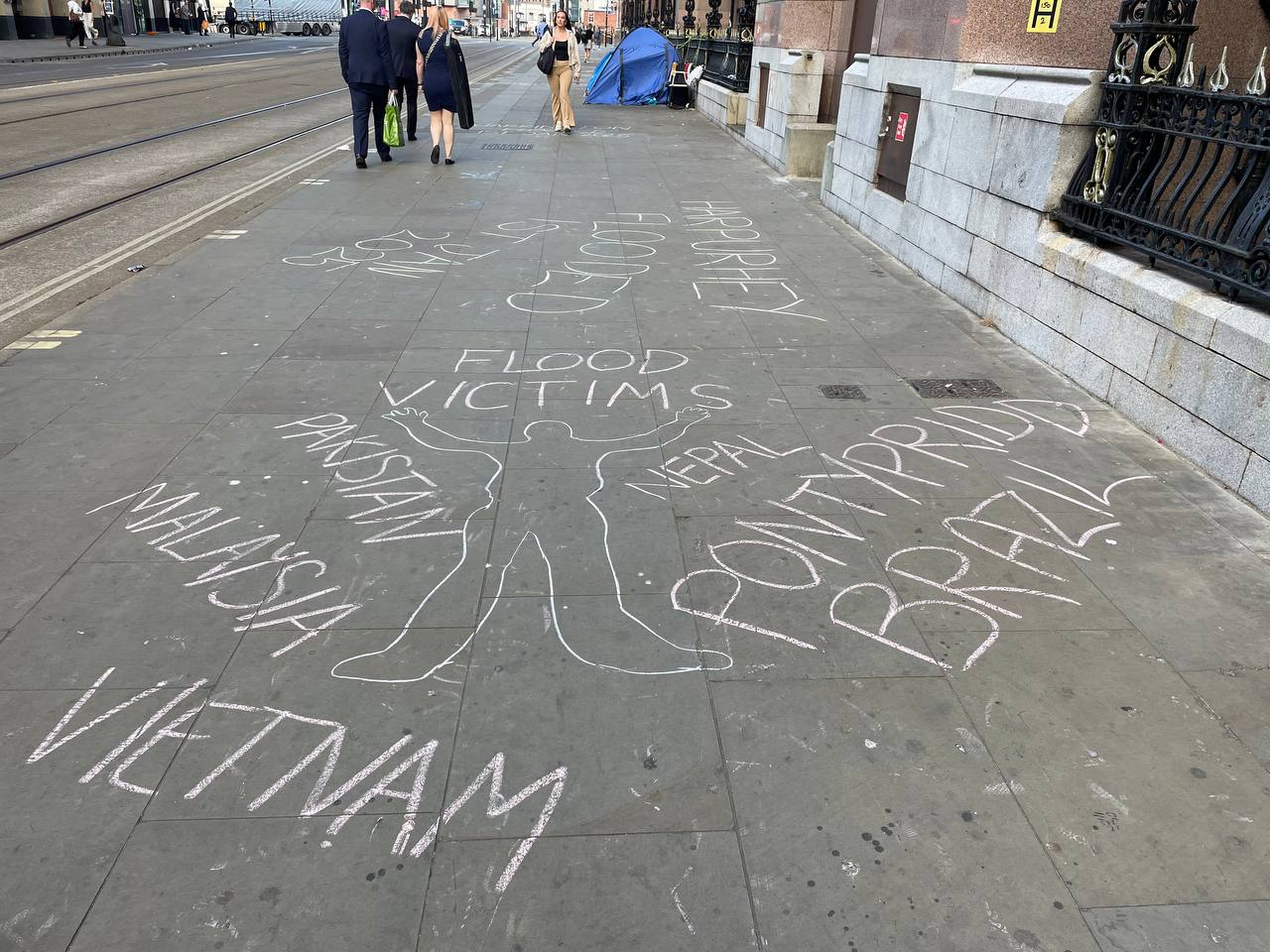 Chalked pavement with a body shape outline and words reading: Flood victims, Pakistan, Malaysia, Vietnam, Nepal, Pontypridd, Brazil.