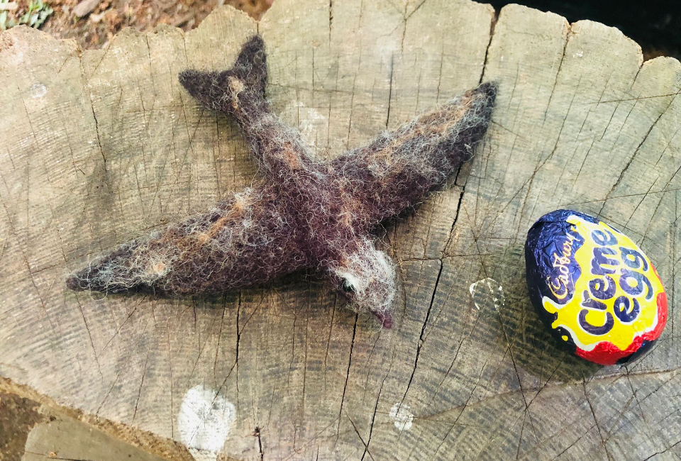 Felted swift on a tree stump next to a Cadbury Creme Egg. 