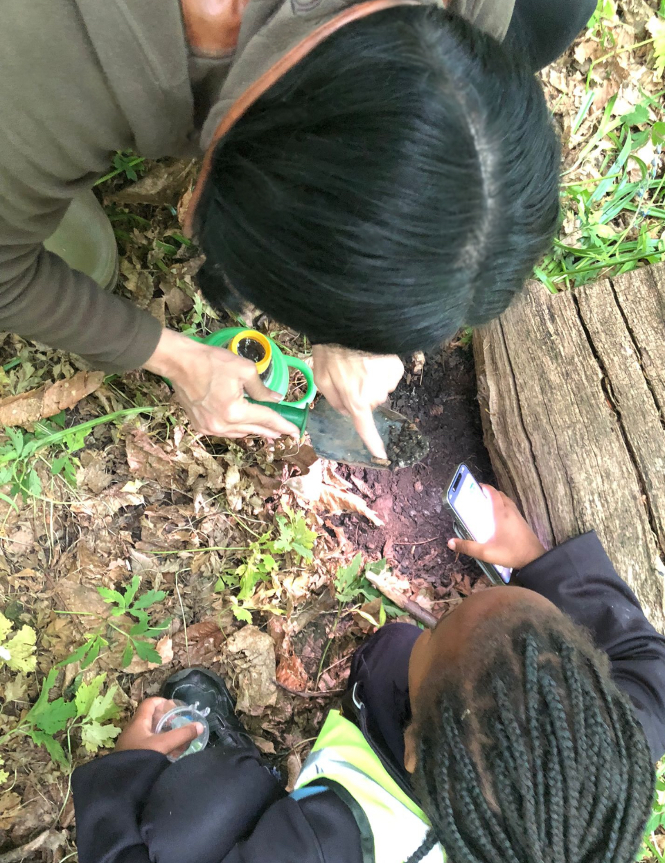Carly Ahlen and a student investigating insects in a piece of bark on the forest floor. 