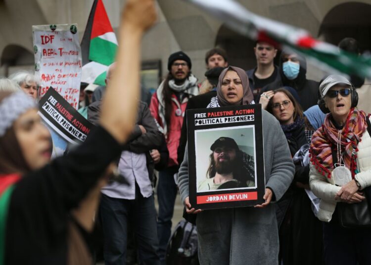 Protesters outside a Filton 18 court trial with Palestine flags and placards reading "Free Palestine Action Political Prisoners" with pictures of Filton 18 activists such as Jordan Devlin.