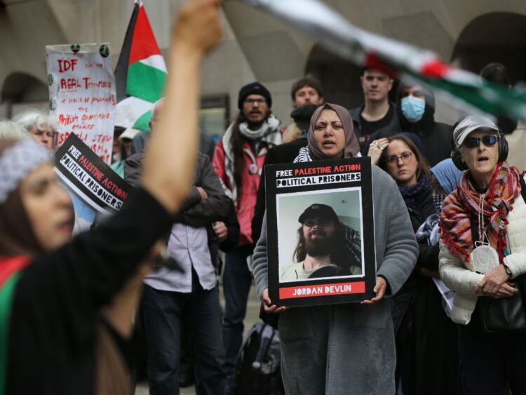 Protesters outside a Filton 18 court trial with Palestine flags and placards reading "Free Palestine Action Political Prisoners" with pictures of Filton 18 activists such as Jordan Devlin.