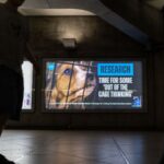 Billboard at Platform 2, Eastbound on the District Line at Westminster Station with a beagle puppy peering out from behind bars and text reading: Research. Time for some 'out of the cage thinking' with PETA's logo.