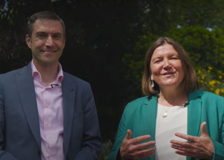 Left: Adrian Ramsay smiling in a suit and pink shirt. Right: Ellie Chowns speaking in a green blazer and cream blouse. Backdrop of greenery. Green Party leadership election
