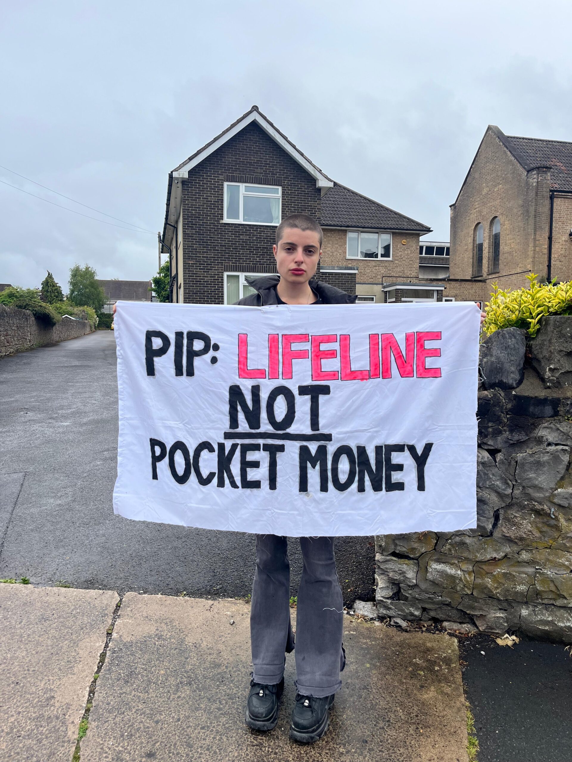 Gigi outside town hall with a banner reading: "PIP: Lifeline not pocket money". DWP PIP