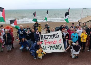 Group of people at the beach holding Palestine flags and a banner reading: "Hastings Friends of Al-Mawasi". Hastings