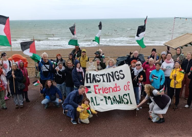 Group of people at the beach holding Palestine flags and a banner reading: "Hastings Friends of Al-Mawasi". Hastings