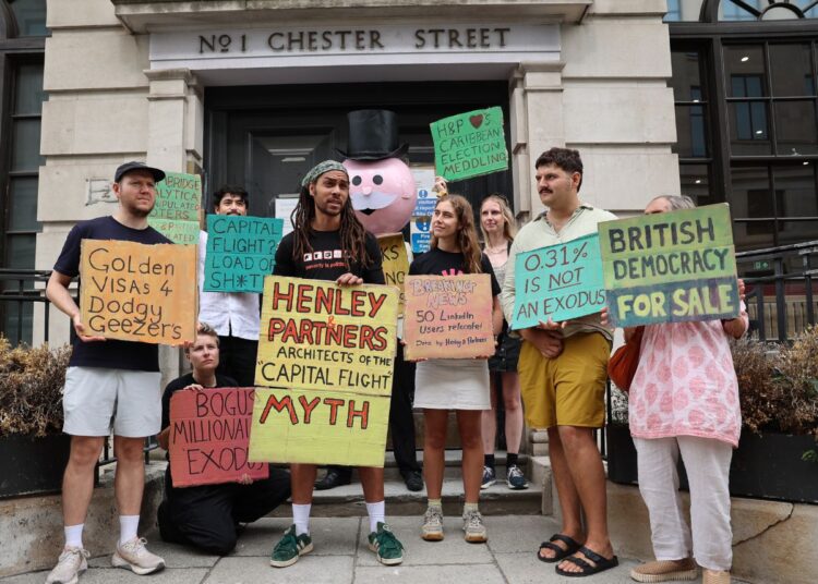 Protesters standing with Mr Monopoly outside Henley and Partners, holding placards reading: "Capital flight? Load of Sh*te", "Henley & Partners - Architects of capital flight myth", "Thanks for fudging the numbers", "Bogus millionaire exodus", "H&P loves Caribbean election meddling", "Democracy for sale", and "Cambridge Analytica manipulated voters. Henley & Partners manipulated the data."