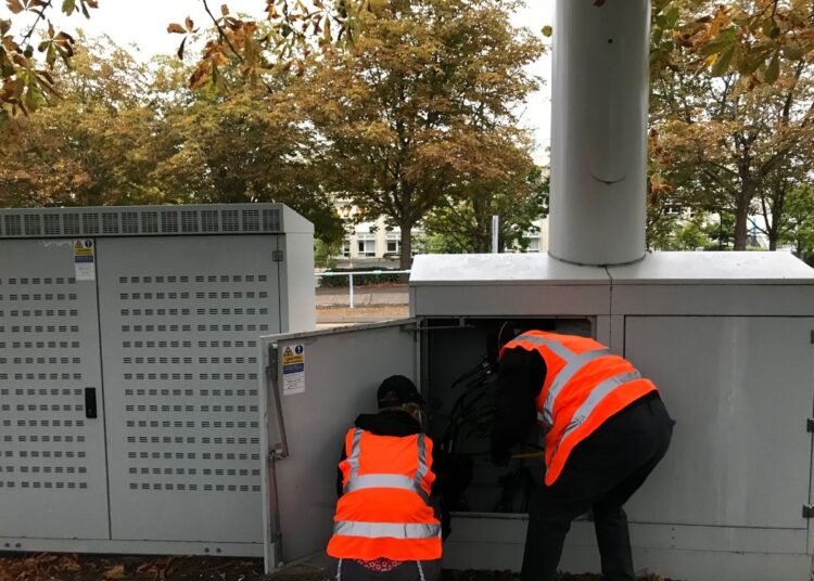 Two activists in high-vis vests leaning into an electrical services cabinet to cut cables JP Morgan