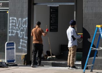 Two workers clean the entrance to Eagle Strategic Consulting where activists shattered windows and graffitied overnight DISMANTLE