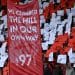 Hillsborough - people hold up red and white pieces of paper and a fabric banner with the words ' We climbed the hill in our own way - 97' to commemorate the 97 victims of the hillsborough disaster