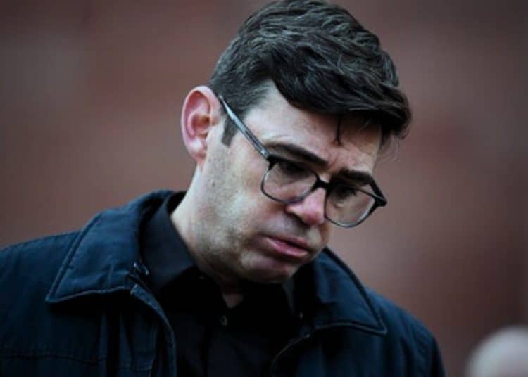 Andy Burnham looking down towards the floor, seemingly in the middle of blowing air out his mouth