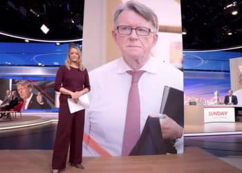 Laura kuenssberg standing in front of a giant picture of Peter Mandelson