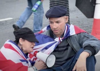 Niko Omilani in a white rubber mask talking to a racist woman at Unite the Kingdom