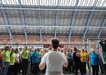 Climate Choir in the station singing together in a large crowd. Person with her back to the photo conducting the choir.