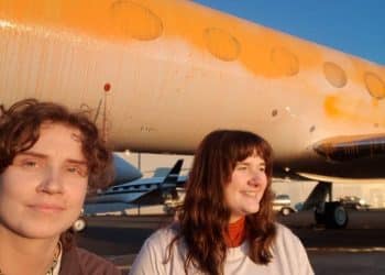 Jennifer Kowalski and Cole Macdonald stand in front of a jet they've spray-painted orange.