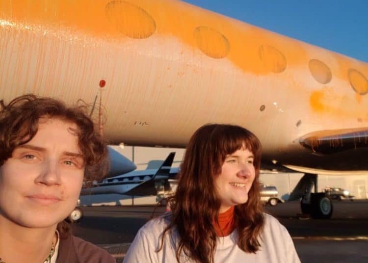 Jennifer Kowalski and Cole Macdonald stand in front of a jet they've spray-painted orange.