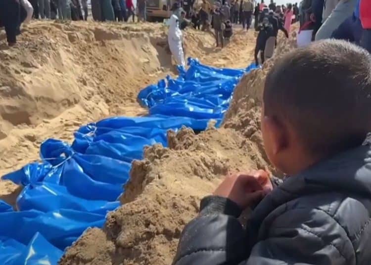 Palestinians bury a long line of bodies in a mass grave in Gaza. A child looks on. Gaza civilians killed
