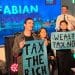 Torsten Bell on stage at the Fabian Reception at Labour's conference, as three activists stand in front of him holding placards reading "Tax the rich" and "Wealth tax now!"