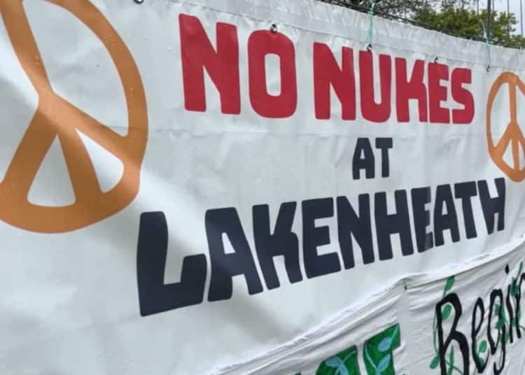 Banner with peace symbols attached to fence that reads: "No nukes at Lakenheath".
